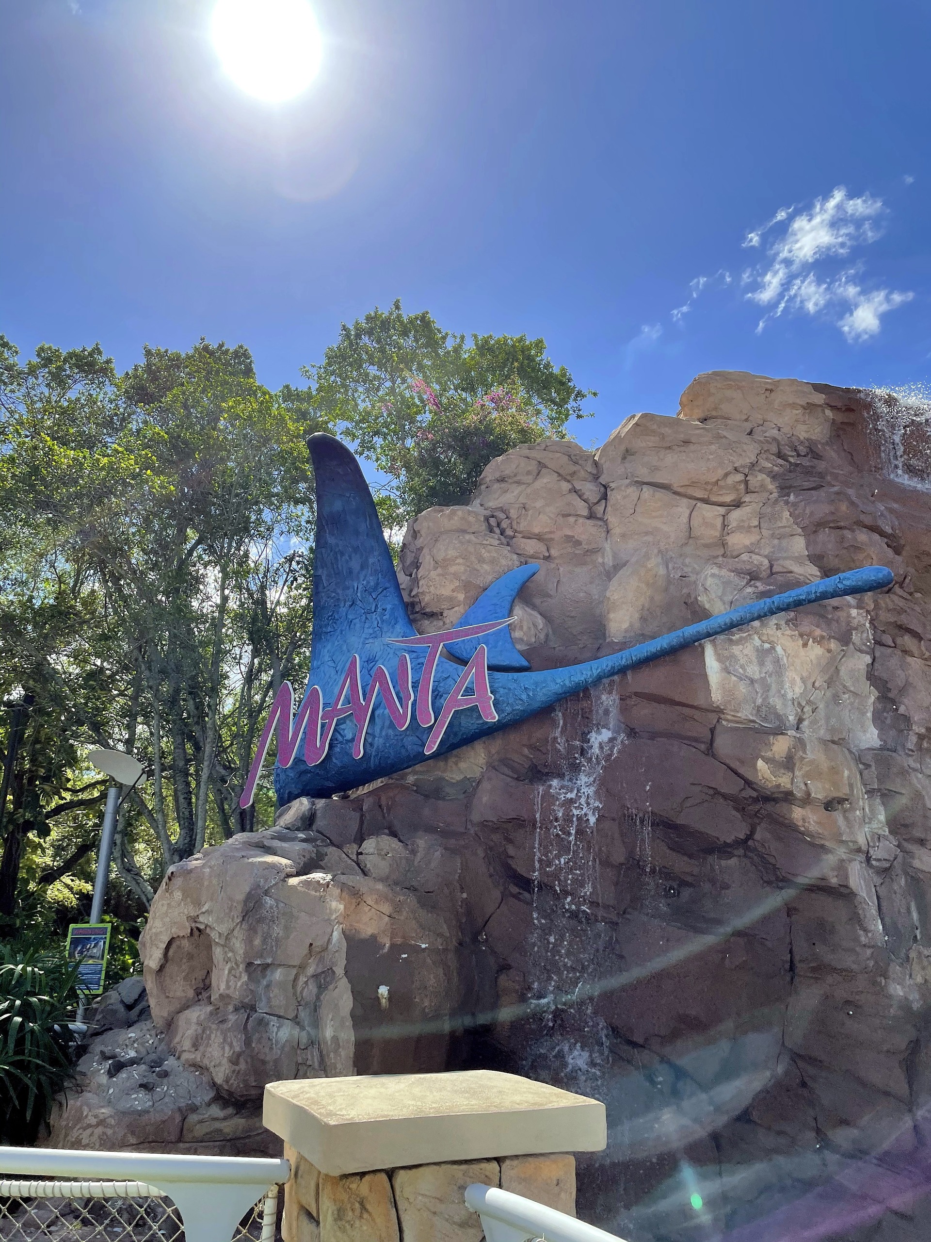 The Manta ray sign on the rock waterfall with the sun flaring above it at SeaWorld Orlando, March 2021
