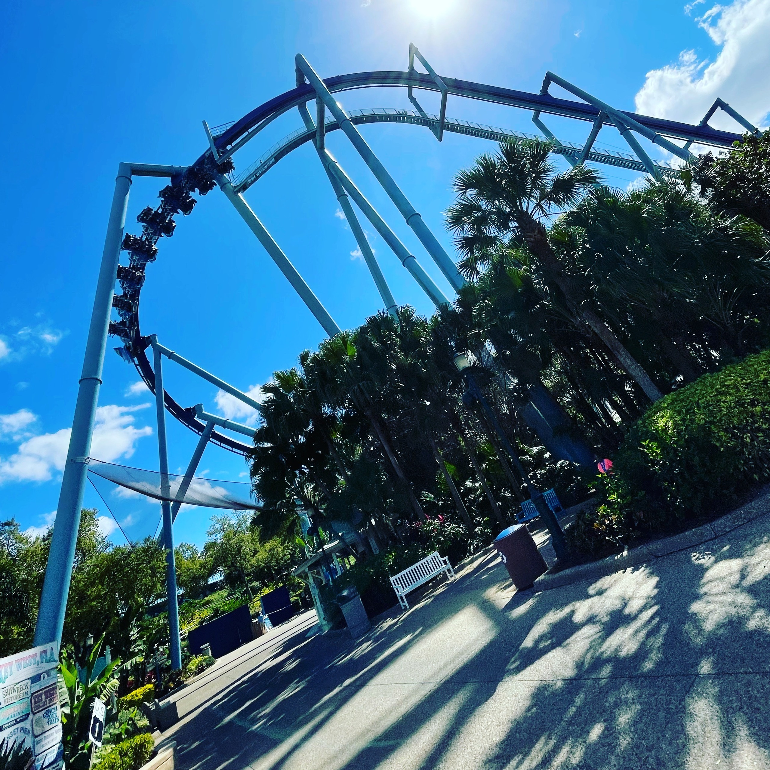 A Manta train riders-down through an inversion on the dark blue track above the walkway at SeaWorld Orlando, March 2021