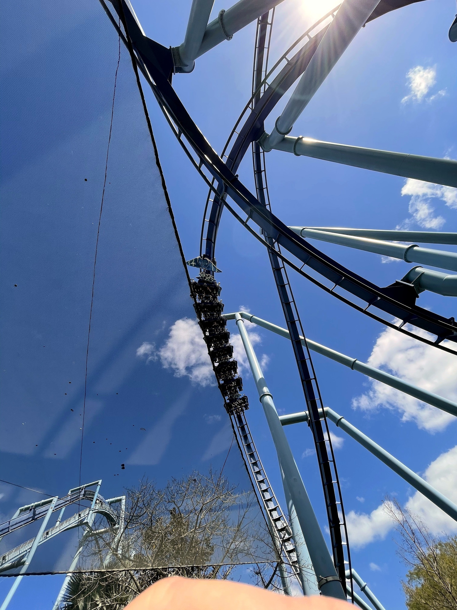 A Manta train crossing overhead between the light blue supports at SeaWorld Orlando, March 2021