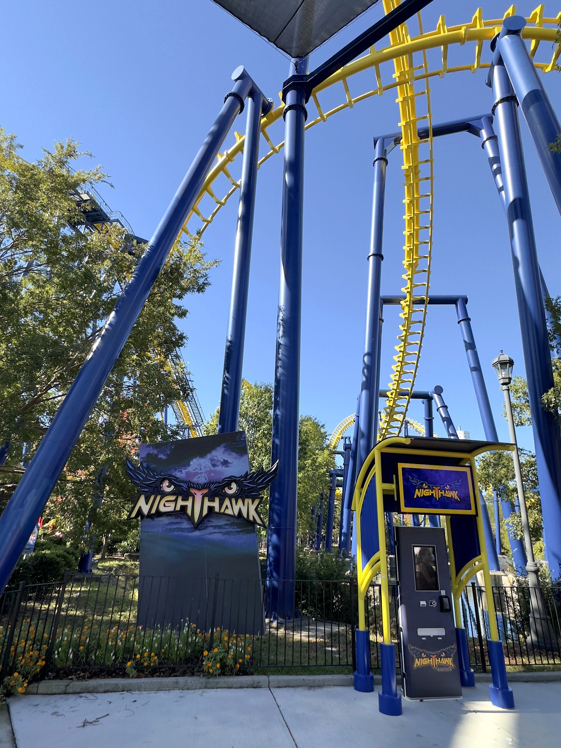 The Nighthawk entrance sign with the yellow track rising between blue supports at Carowinds, October 2024