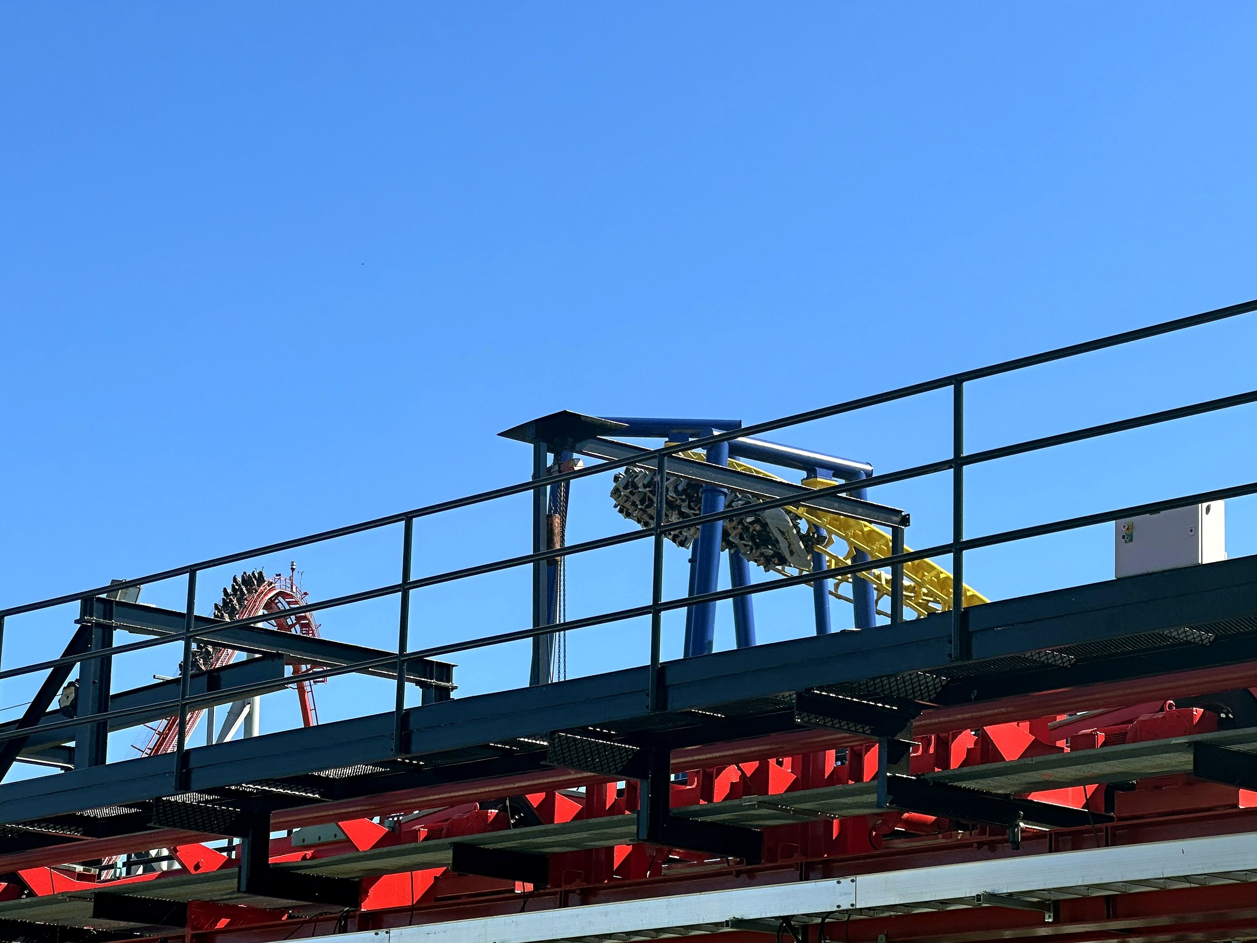 A Nighthawk train on its yellow track seen past a catwalk at Carowinds, October 2024