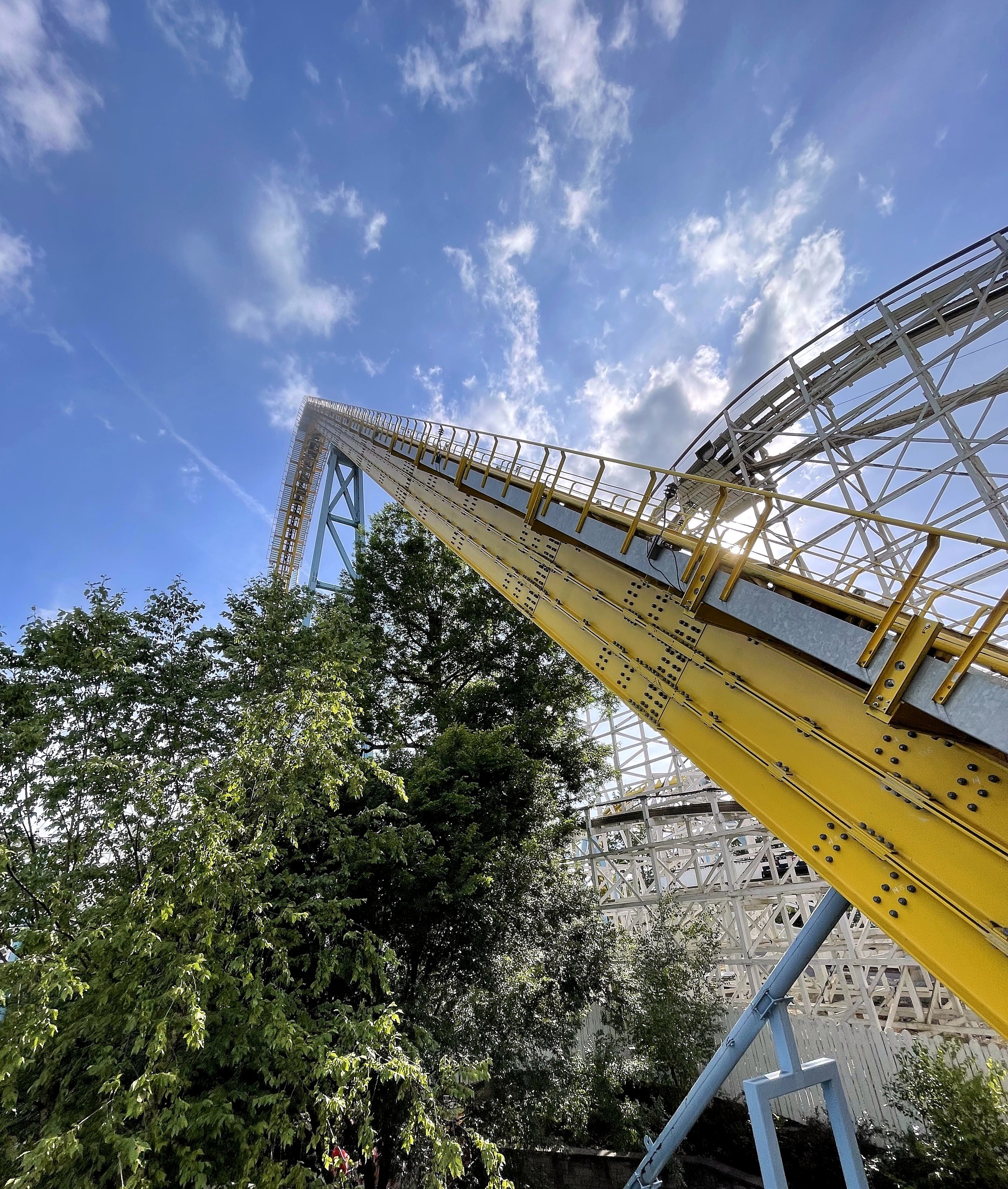 Skyrush's yellow lift hill rising past Comet's white wooden structure at Hersheypark, June 2021
