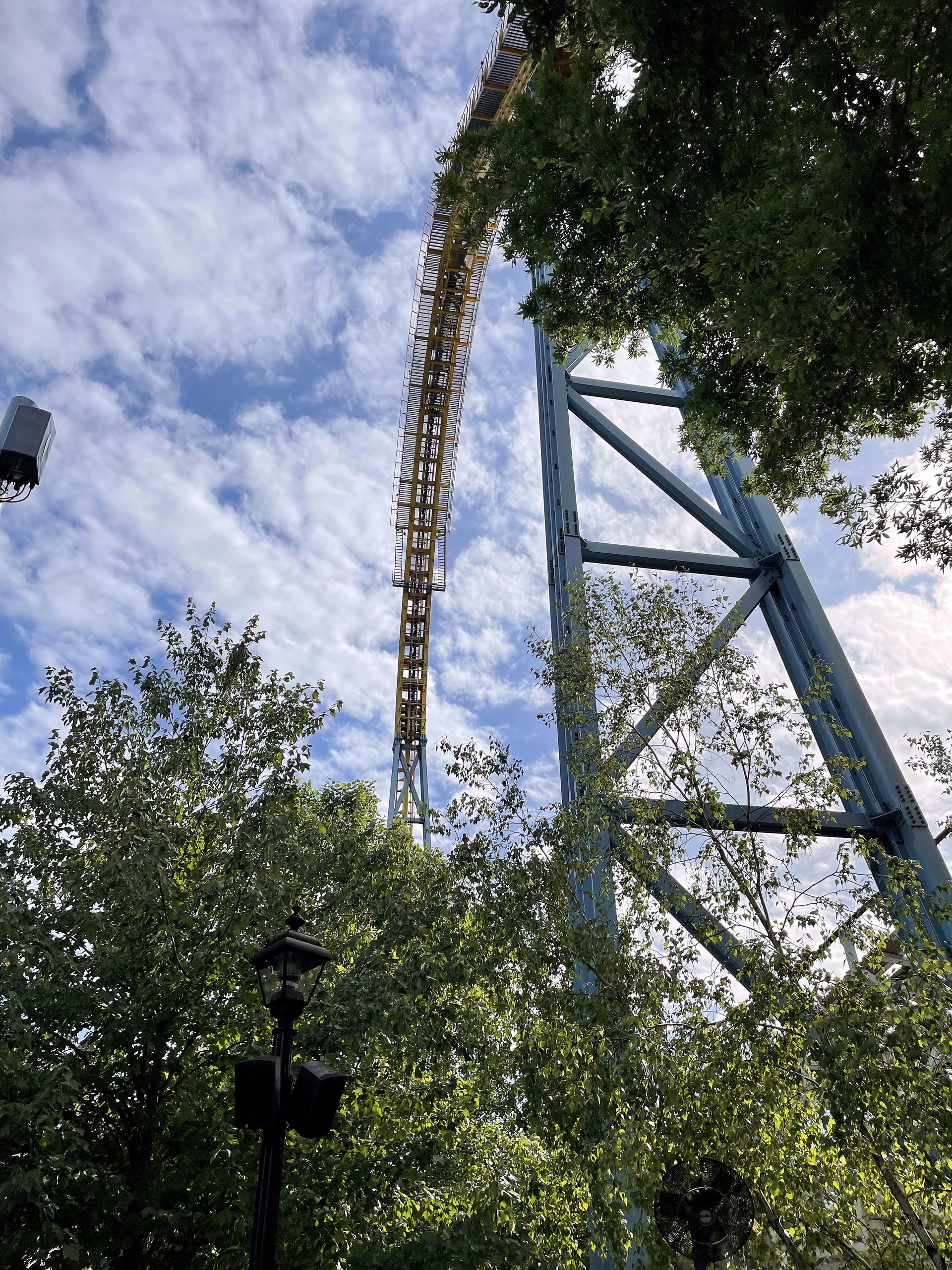 Skyrush's yellow lift hill rising through the trees at Hersheypark, June 2021