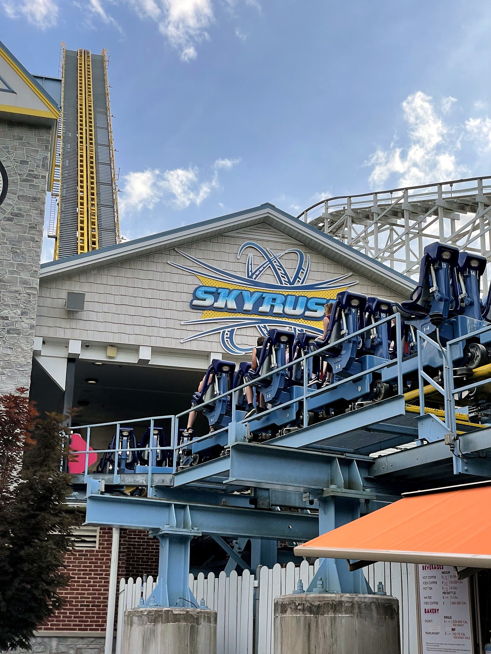 The Skyrush station sign with a train, Comet's wooden structure beside the lift hill at Hersheypark, June 2021