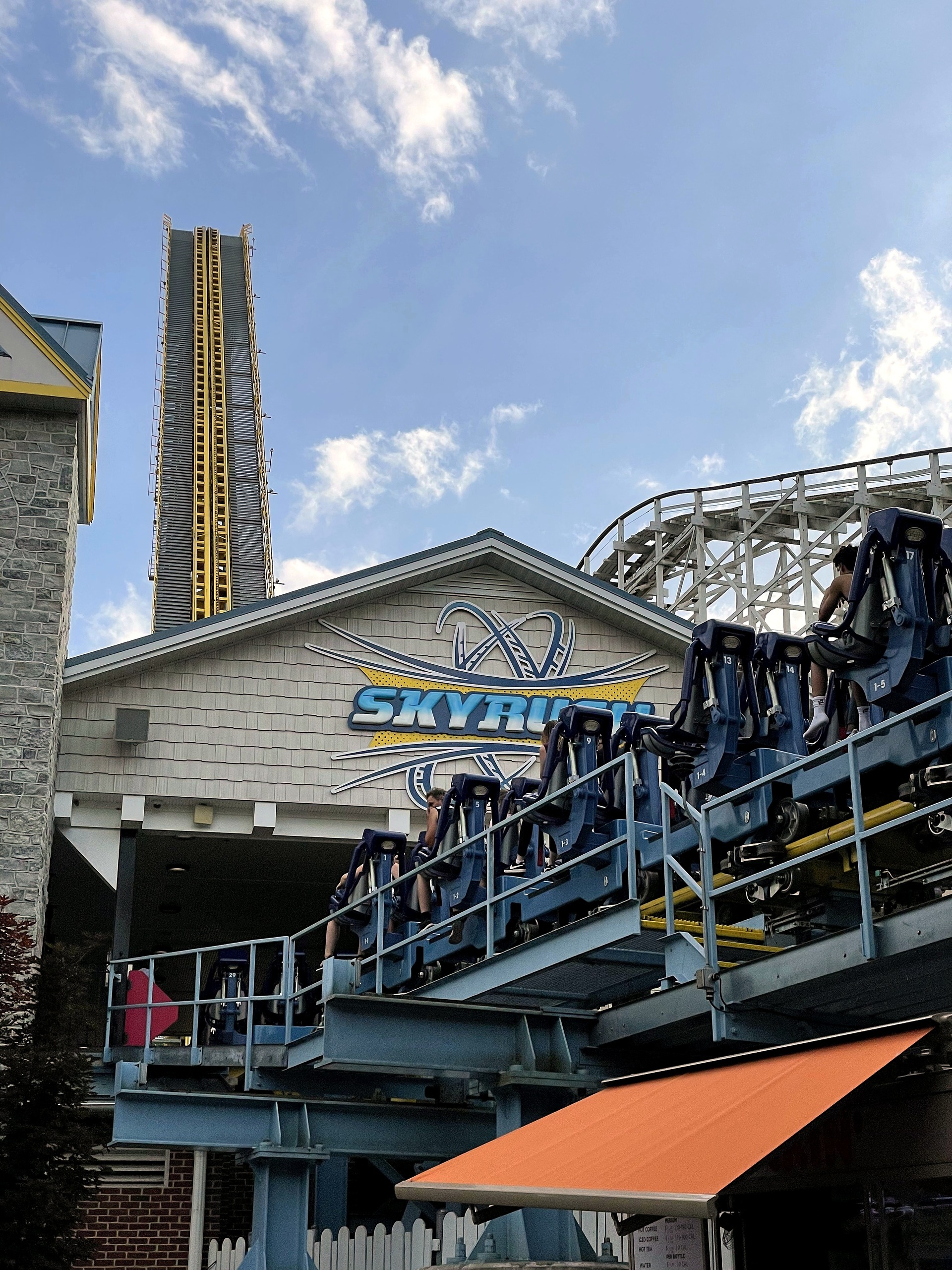 A Skyrush train with riders aboard in the station, the lift hill and Comet behind at Hersheypark, June 2021