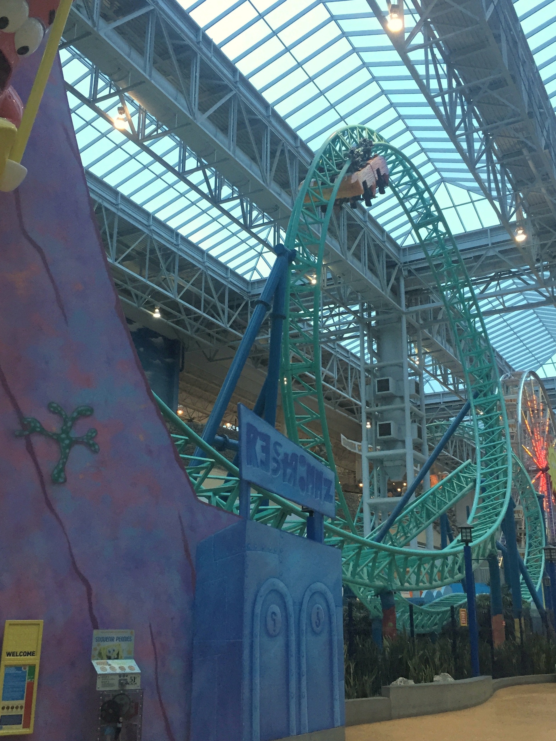 A SpongeBob SquarePants Rock Bottom Plunge train cresting the teal track above the entrance walkway at Nickelodeon Universe, November 2015