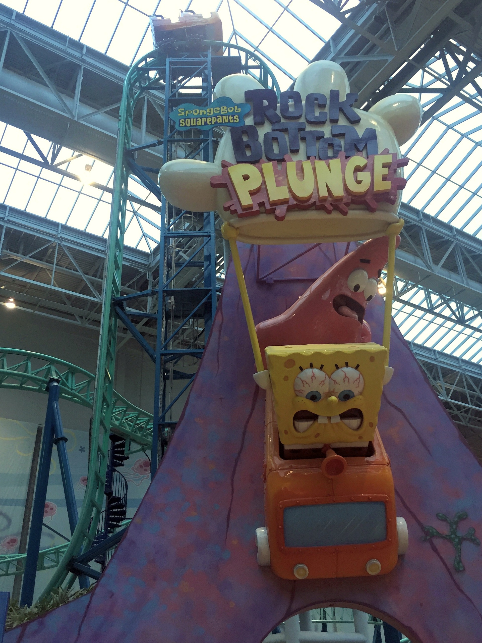 The SpongeBob SquarePants Rock Bottom Plunge entrance sign with a train on the vertical lift behind at Nickelodeon Universe, November 2015