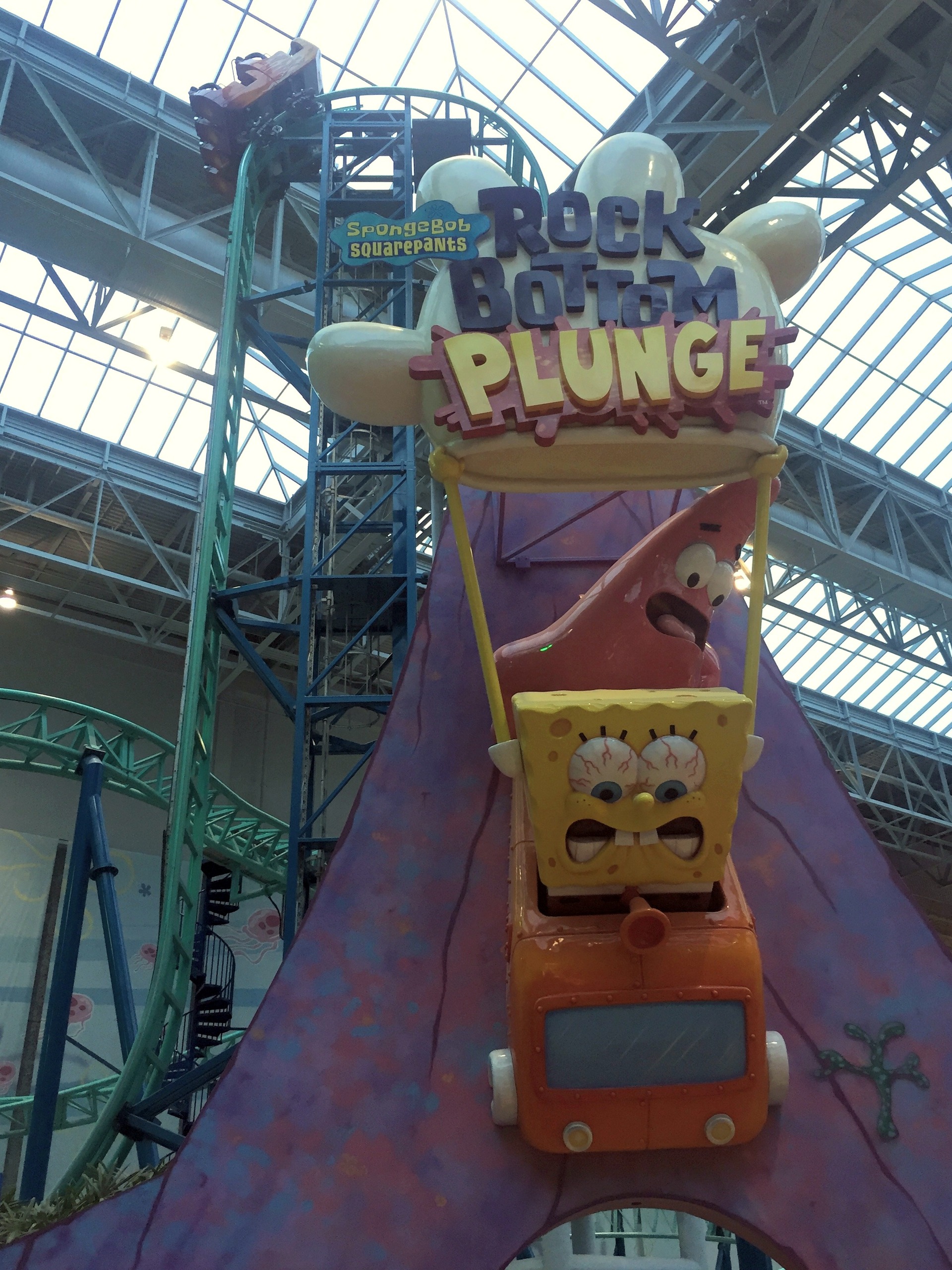 The SpongeBob SquarePants Rock Bottom Plunge sign with a train atop the vertical lift under the skylights at Nickelodeon Universe, November 2015