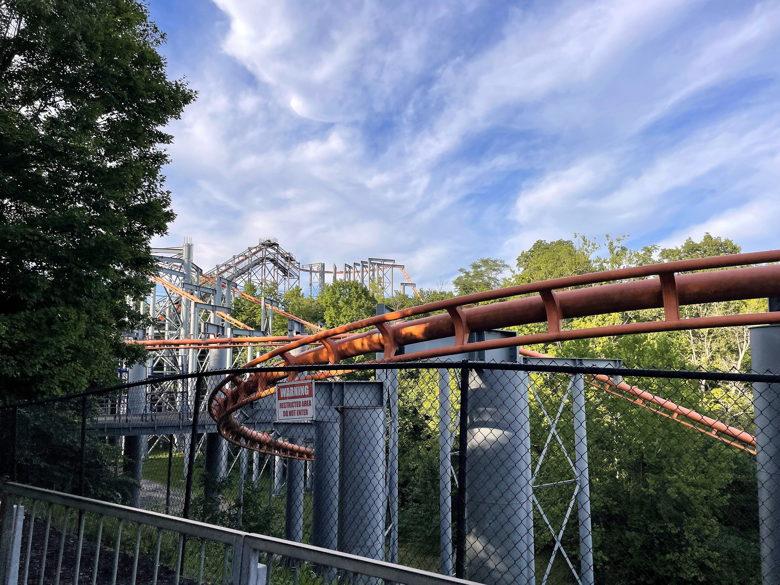 The Bat's orange track curving past the fence with the lift beyond, Kings Island, July 2022