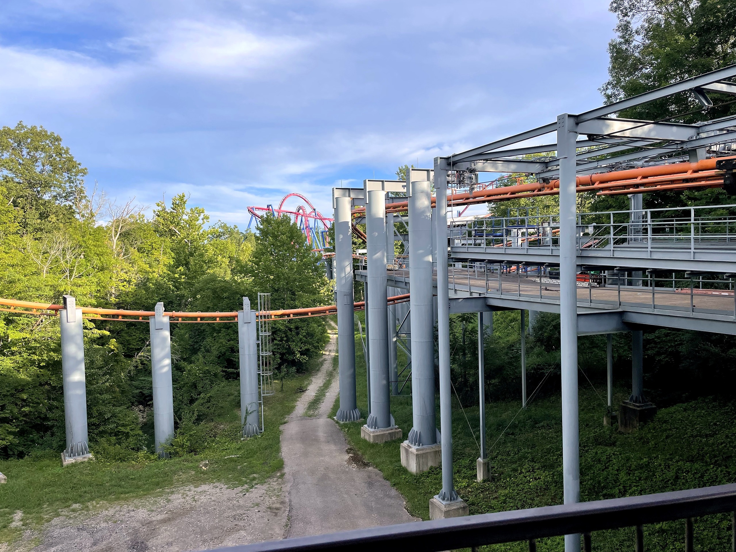 The Bat's gray supports and orange track running into the woods, Kings Island, July 2022