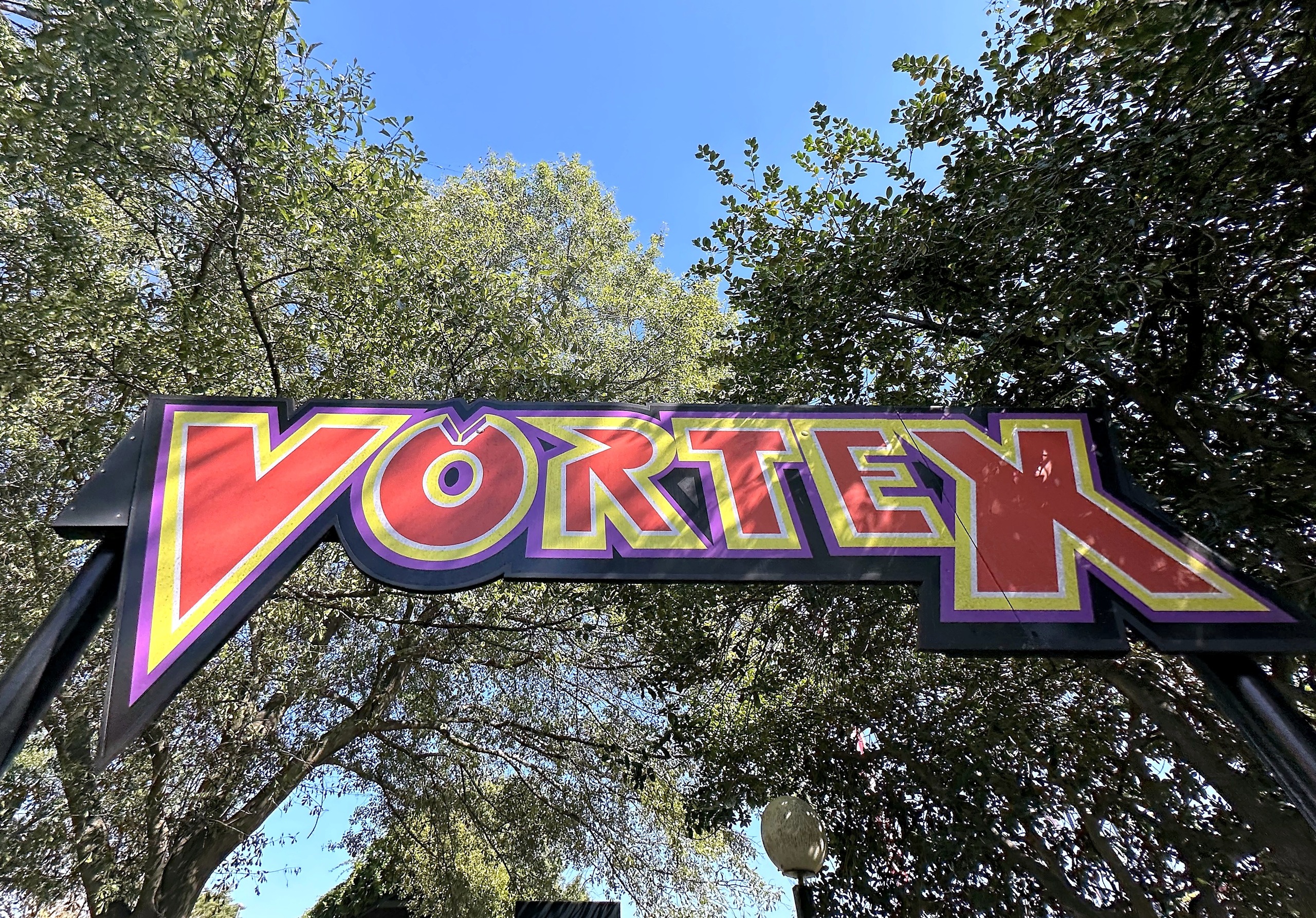 The red and purple Vortex entrance sign under the trees at Carowinds, October 2024